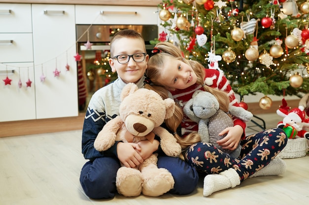 Frère et sœur assis près de sapin de Noël avec des peluches