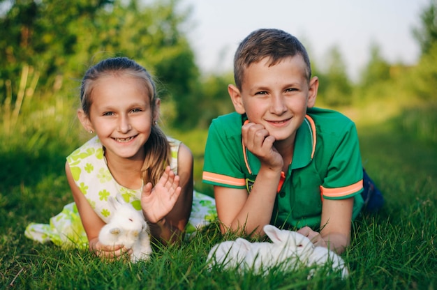 Photo frère et soeur couché sur l'herbe avec des petits lapins. lapin de pâques