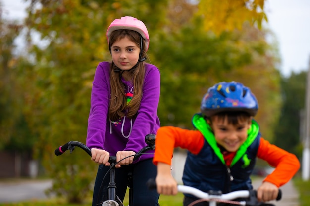 Frère et sœur font du vélo et portent des casques de protection dans le parc de la ville en automne. Sur la photo, les arbres derrière sont flous.