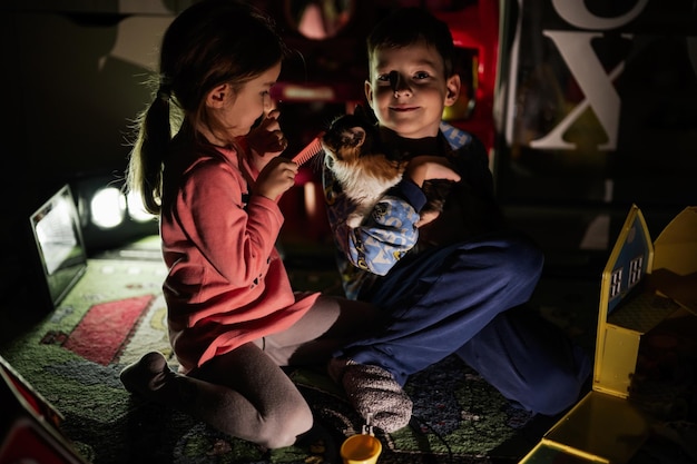 Frère et sœur jouant avec kitty à la maison pendant une panne d'électricité en utilisant un éclairage alternatif