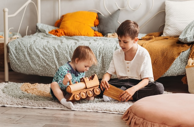 Frère et sœur jouent avec des jouets en bois dans la chambre des enfants. Les enfants jouent avec un créateur de jouets sur le sol.