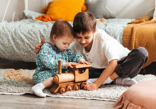 Frère et sœur jouent avec des jouets en bois dans la chambre des enfants. Les enfants jouent avec un créateur de jouets sur le sol.