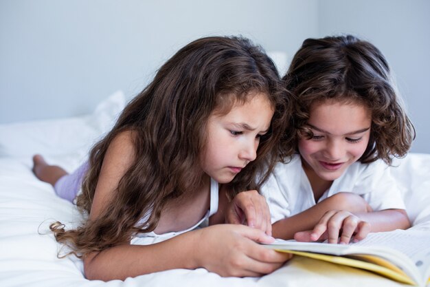 Frère et soeur lisant un livre ensemble sur le lit