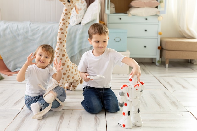 Frère et soeur de petits enfants assis sur le sol dans la pièce, riant et jouant avec le robot