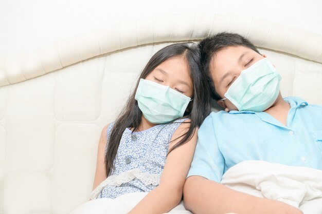 Frère et sœur portent un masque chirurgical sur le lit, enfant malade