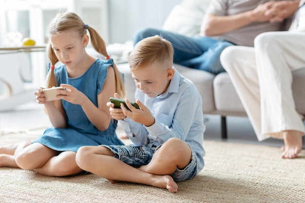 Frère et sœur avec des smartphones assis par terre dans le salon