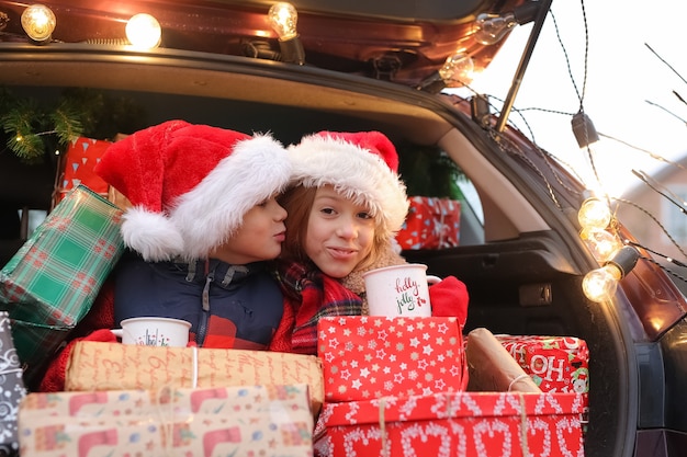 Photo frère et sœur sont assis dans la voiture décorée du nouvel an avec beaucoup de coffrets cadeaux