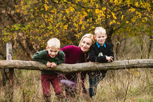 Frères blonds jumeaux préadolescents jouant à l'extérieur avec une mère célibataire heureuse dans un magnifique parc d'automne chaud, week-end en famille dans la nature