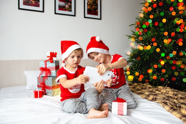 Les frères en chapeaux de Père Noël regardent une tablette et choisissent des cadeaux