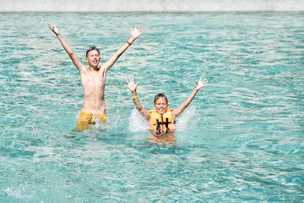 Des frères heureux se tiennent dans la piscine avec de l'eau bleue levant les mains
