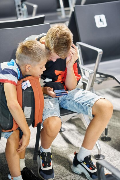 Les frères jouent à des jeux et partagent leurs intérêts en utilisant des smartphones dans la salle d'attente avec des fauteuils à l'aéroport