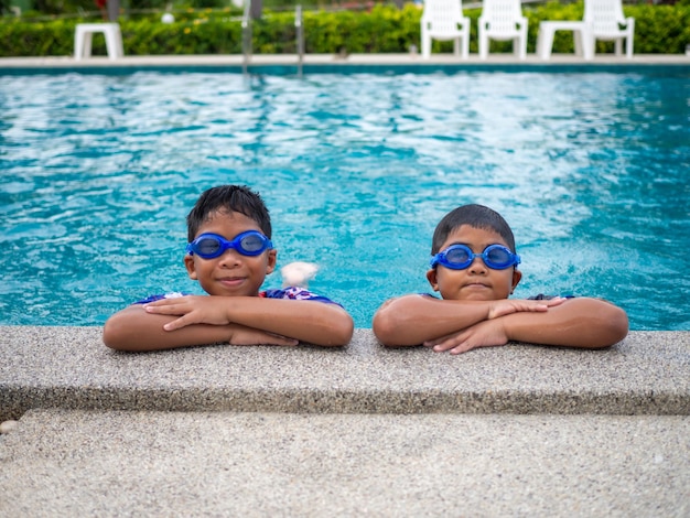 Frères portant des maillots de bain et des lunettes Souriez tout en étant perchés au bord de la piscine