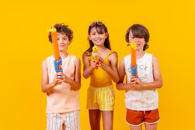 Frères s'amusant avec des pistolets à eau pendant les vacances d'été et visant le fond jaune de la caméra