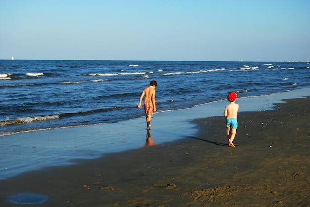 Des frères sans chemise marchant sur le rivage à la plage