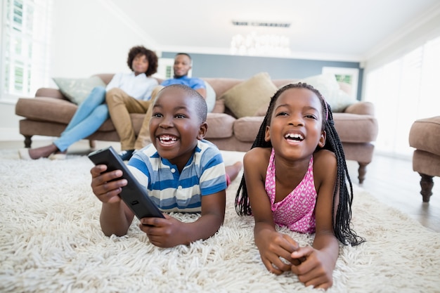 Frères et sœurs allongé sur un tapis et regarder la télévision dans le salon