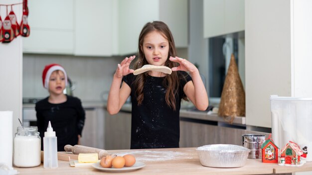 Les frères et sœurs cuisinent dans la cuisine, le garçon avec un chapeau de Noël, la fille vomit la pâte. Idée d'enfants heureux