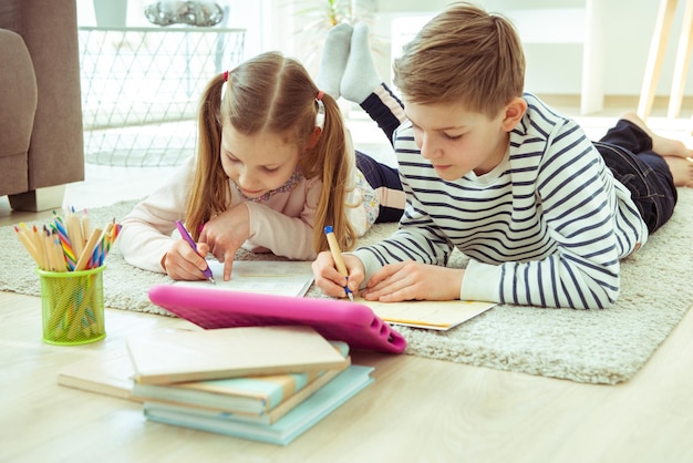 Des frères et sœurs écrivant sur du papier alors qu'ils sont allongés à la maison.