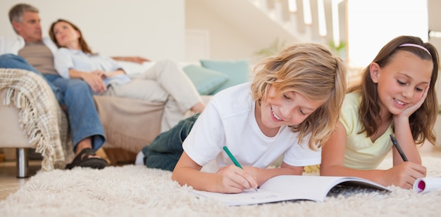 Frères et sœurs faisant leurs devoirs sur le tapis avec les parents derrière eux