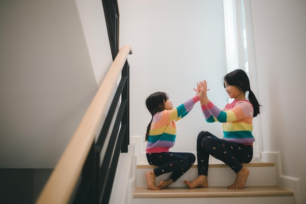 Frères et sœurs filles asiatiques jouant des ciseaux à papier de roche jeu de main enfants assis dans les escaliers à la maison jouant ensemble