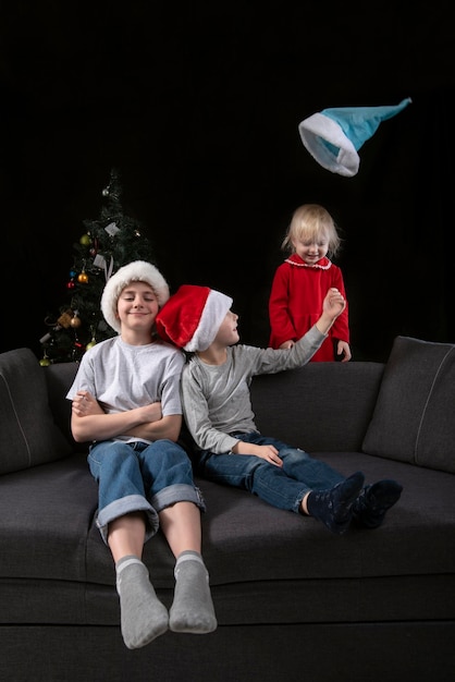 Frères et sœurs à la maison sur le canapé la veille de Noël. Des enfants heureux jouent et jettent leur chapeau.