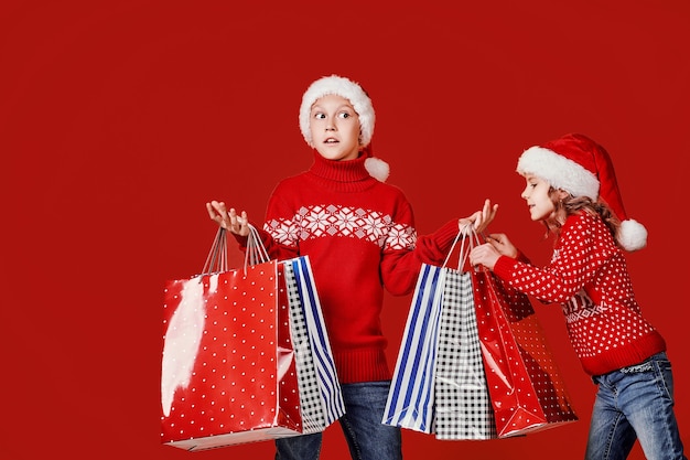 Frères et sœurs mignons en pull rouge tenant des sacs à provisions