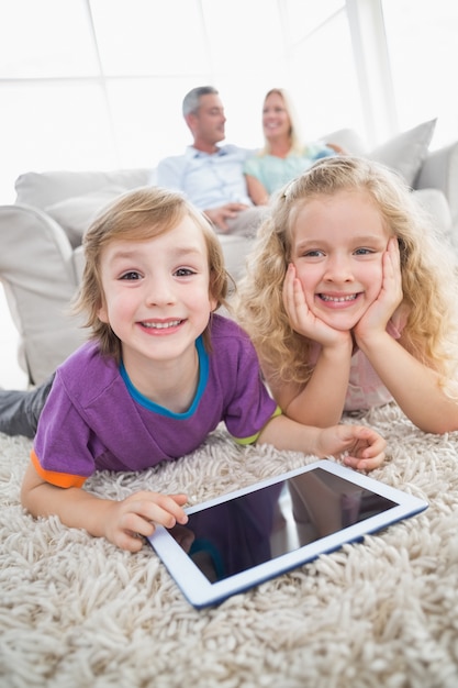 Frères et sœurs avec tablette numérique couché sur le tapis