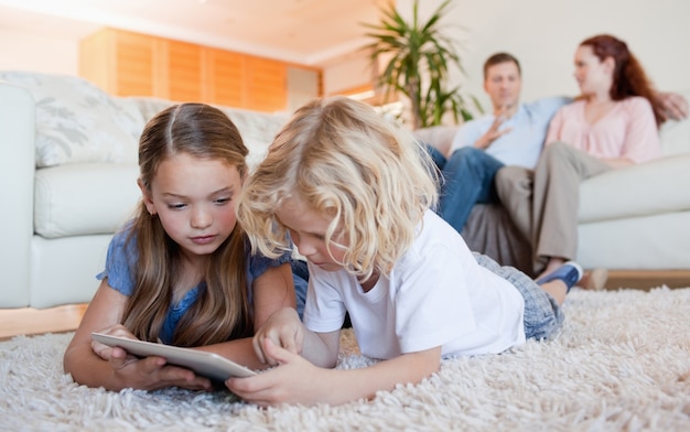 Frères et sœurs utilisant une tablette sur le plancher du salon