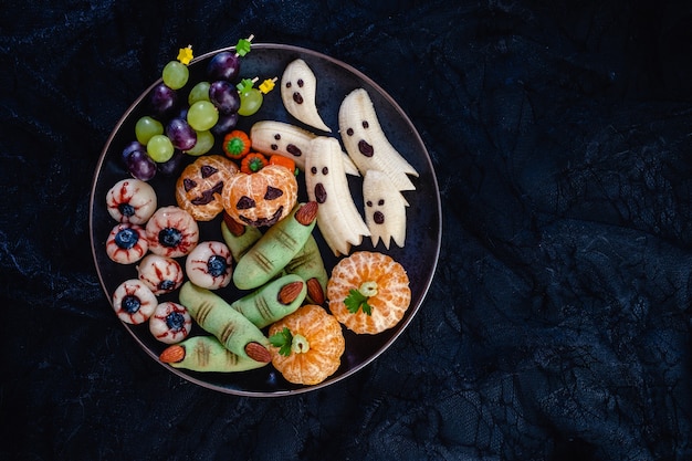 Photo friandises d'halloween aux fruits sains. fantômes de banane, citrouilles orange clémentine, yeux de litchi et biscuits verts de sorcière