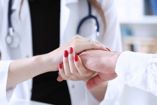 Friendly female doctor hold male patient hand in office