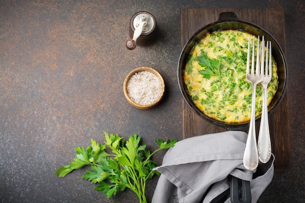 Fritatta avec pommes de terre, pois verts et herbes dans une poêle en fer sur une surface en béton foncé