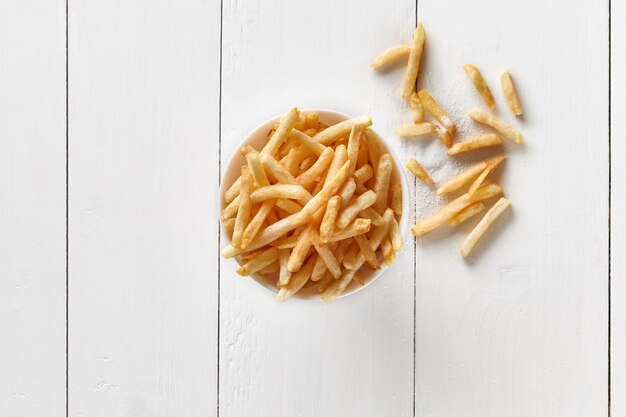 Frites croustillantes dans un bol sur une table en bois blanc