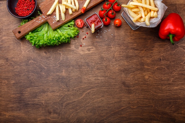 Photo frites dans une grille avec du ketchup, de la salade et des tomates cerises sur une table en bois marron