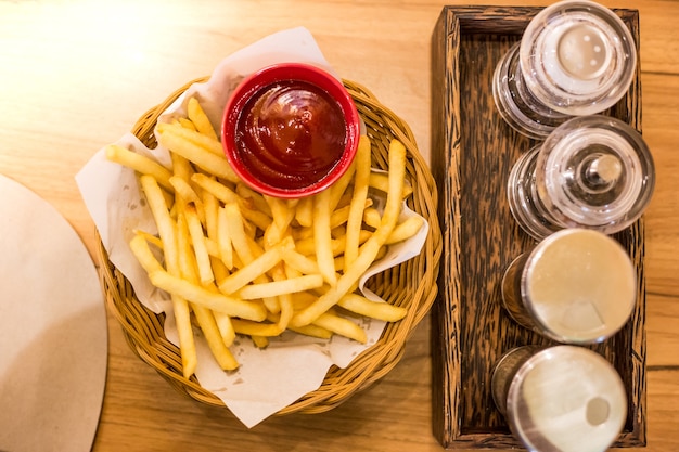 Frites dans un panier en bois avec sauce et épices sur la table.