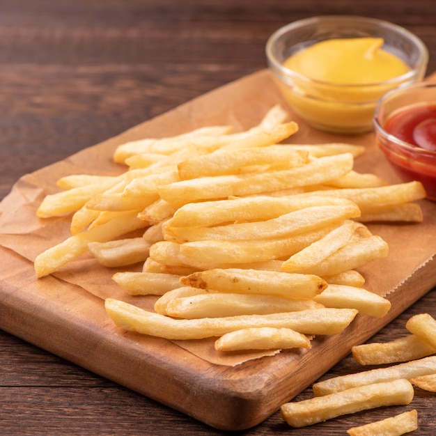 Des frites dorées délicieuses sur papier de cuisson kraft et un plateau de service pour manger avec du ketchup et de la moutarde jaune.