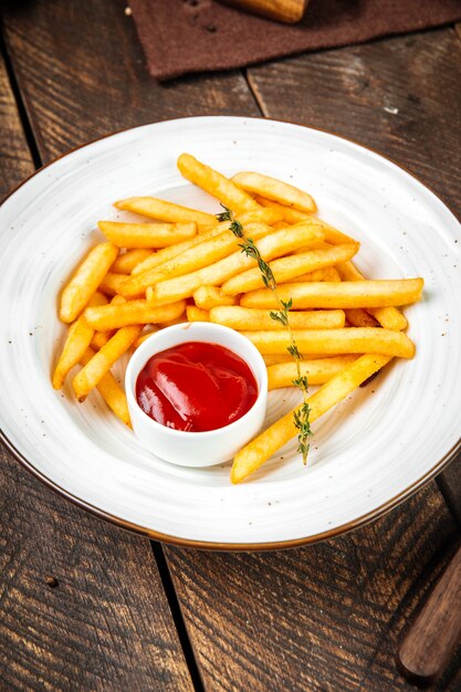 Frites avec du ketchup sur une plaque blanche sur la table en bois