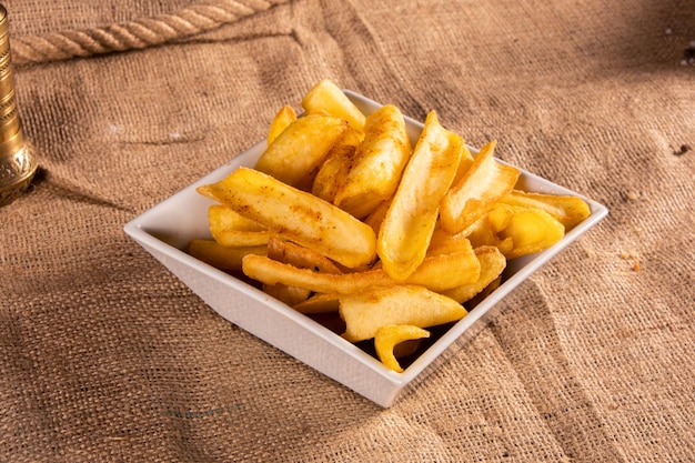 Photo frites fraîches aux épices sur fond d'osier plaque blanche carrée