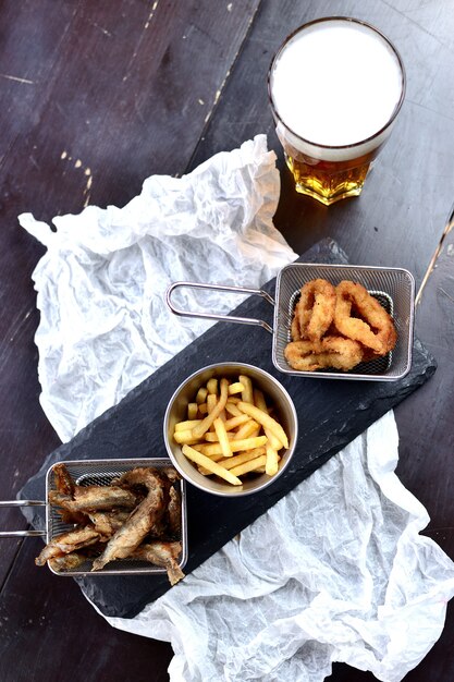 Frites frites, poisson frit et rondelles d&#39;oignon en pâte sur une planche de bois, avec un verre de bière. Bière Snacks