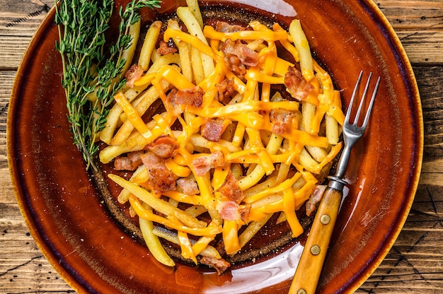 Frites avec fromage cheddar fondu et bacon servis dans une assiette rustique. fond en bois. Vue de dessus.