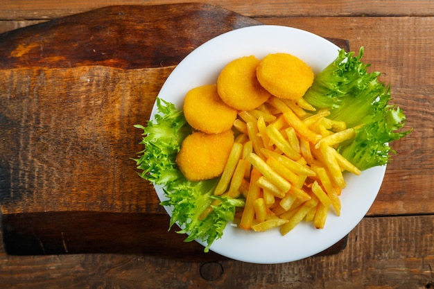 Frites avec pépites de poulet dans une assiette avec salade sur une table en bois sur un support