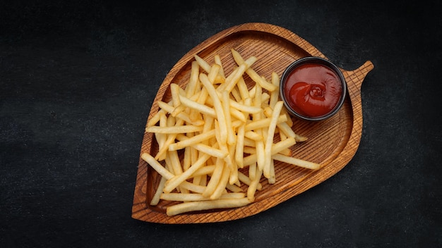 Frites avec sauce sur une planche de bois sur fond noir