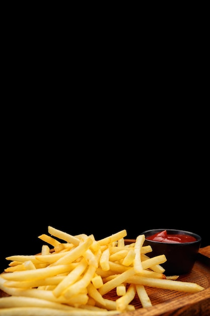 Frites avec sauce sur une planche de bois sur fond noir