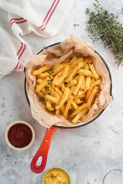 Frites savoureux serveur de frites dans une poêle en fonte rouge avec sauce tomate et fromage sur fond de béton gris ancien Divers plats Keto Restauration rapide et concept d'aliments malsains