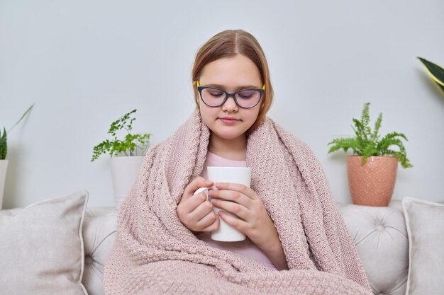 Froide saison automne hiver à la maison adolescente sous couverture assise sur un canapé avec une tasse