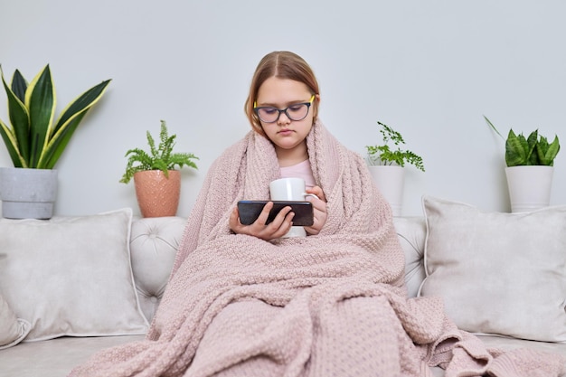 Froide saison automne hiver à la maison adolescente sous couverture assise sur un canapé avec une tasse