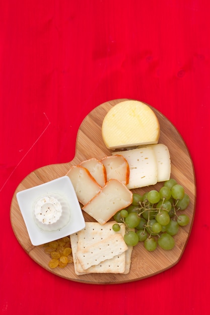 Photo fromage avec des biscuits, raisins sur plateau coeur en bois rouge