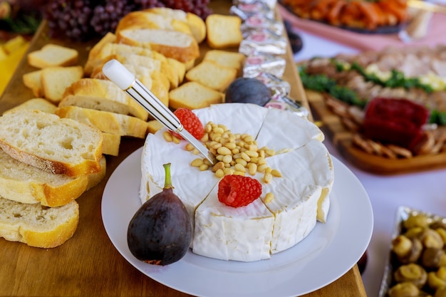 Fromage brie aux noix, pain et fruits. sur une table rustique en bois.