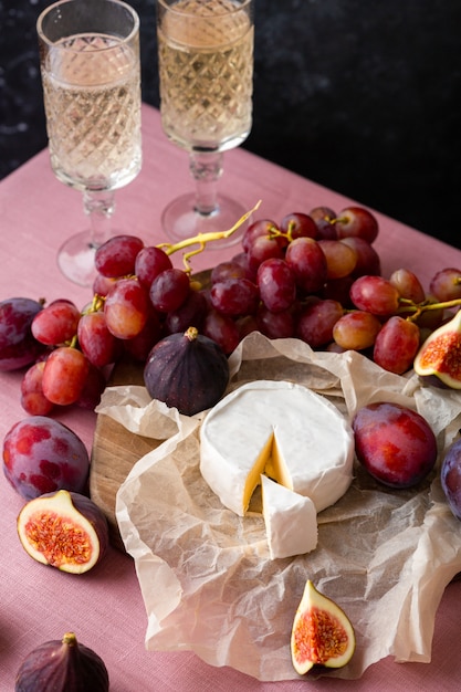 Photo fromage brie sur papier parchemin avec figues, prunes et raisin et champagne sur fond