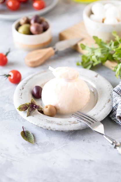 Fromage burrata italien sur une assiette blanche ronde et ingrédients pour salade