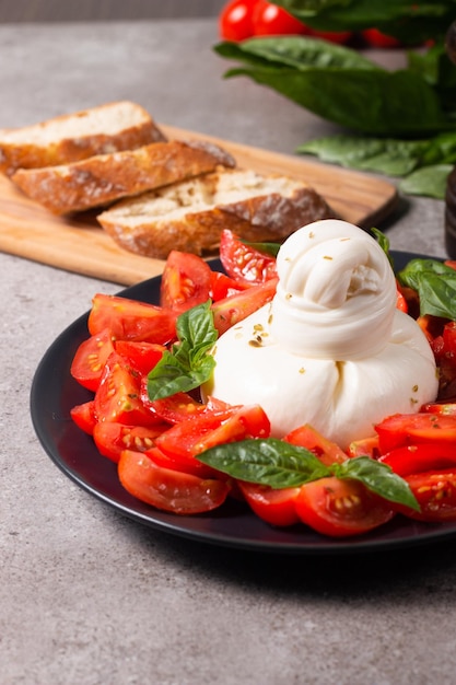 Fromage burrata italien traditionnel avec salade de délicieuses tomates cerises, feuilles de basilic et huile d'olive