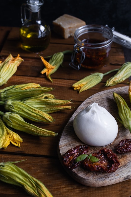 Fromage Burrata, tomates séchées, fleurs de courgettes et huile d'olive sur table en bois rustique